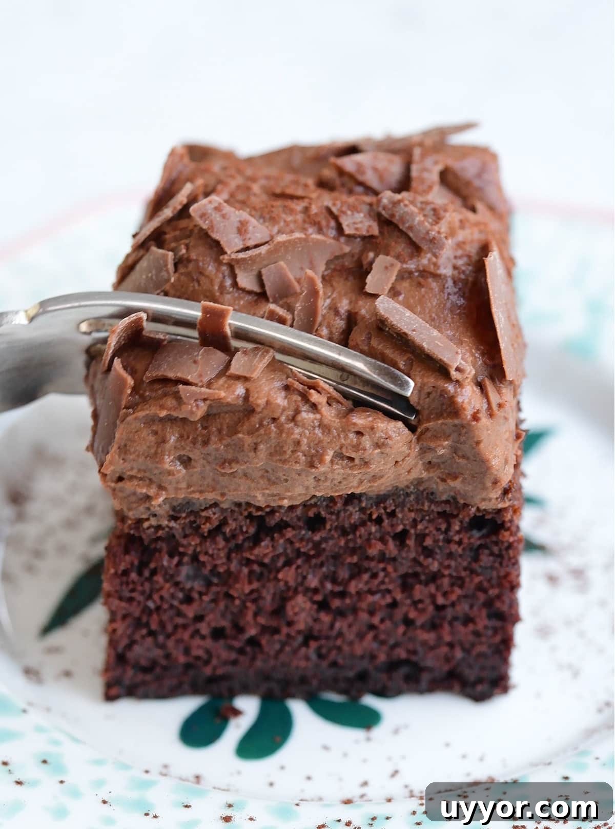 Slice of chocolate banana cake with chocolate frosting on a plate with a form cutting through