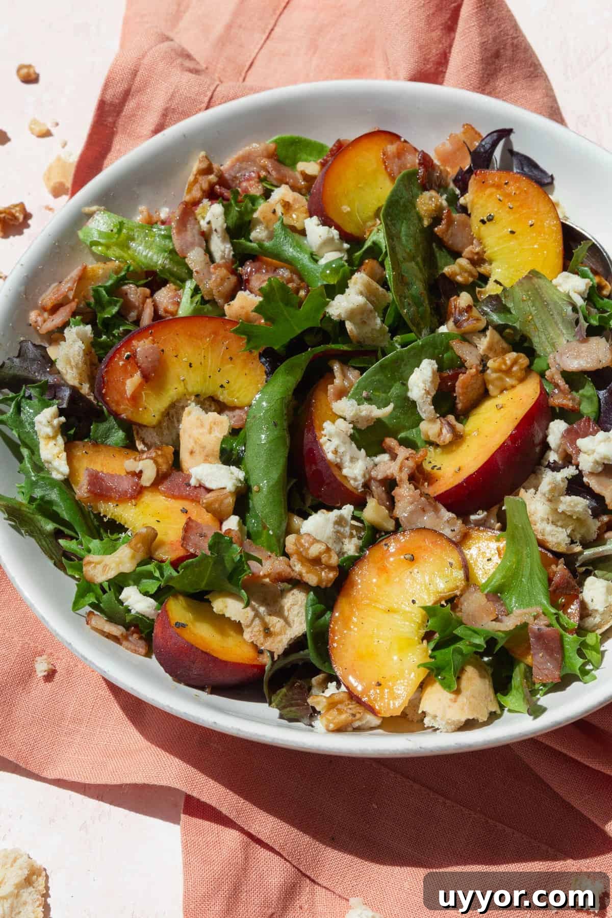 Fresh Peach Salad with Honey-Lime Dressing Recipe 3 Peach salad with baby greens, cheese, and walnuts in a white bowl on a pink napkin.