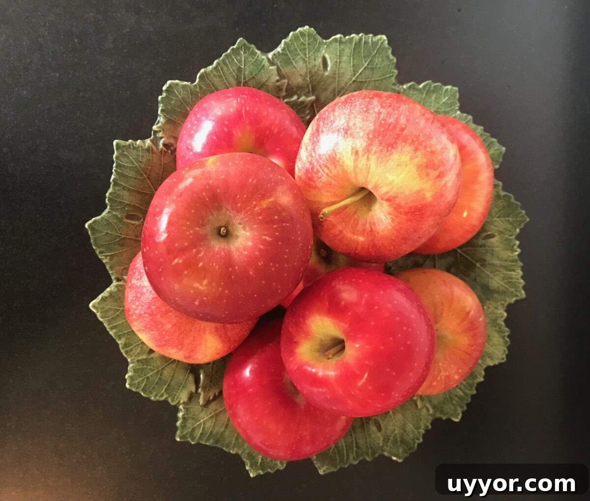 Green leafy ceramic pedestal dish with an assortment of fresh apples on top.