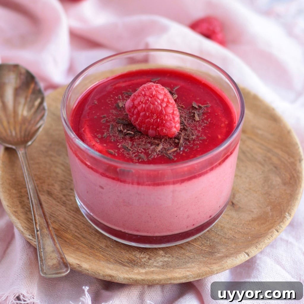 Close up on a Mousse Cup with chocolate shavings and a fresh raspberry, placed over a wooden plate.