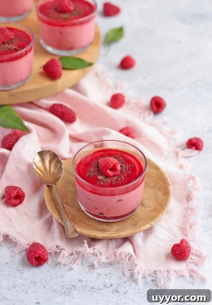 Dessert topped with Chocolate Shavings and a fresh Raspberry on a wooden plate over a pink napkin.
