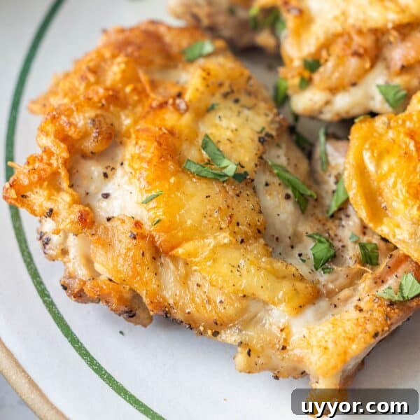 Crispy Honey Mustard Baked Chicken Drumsticks Recipe 12 Close-up of pan fried chicken thighs with crispy golden skin, seasoned with black pepper and garnished with chopped fresh herbs on a white plate—a delicious keto fried chicken recipe.