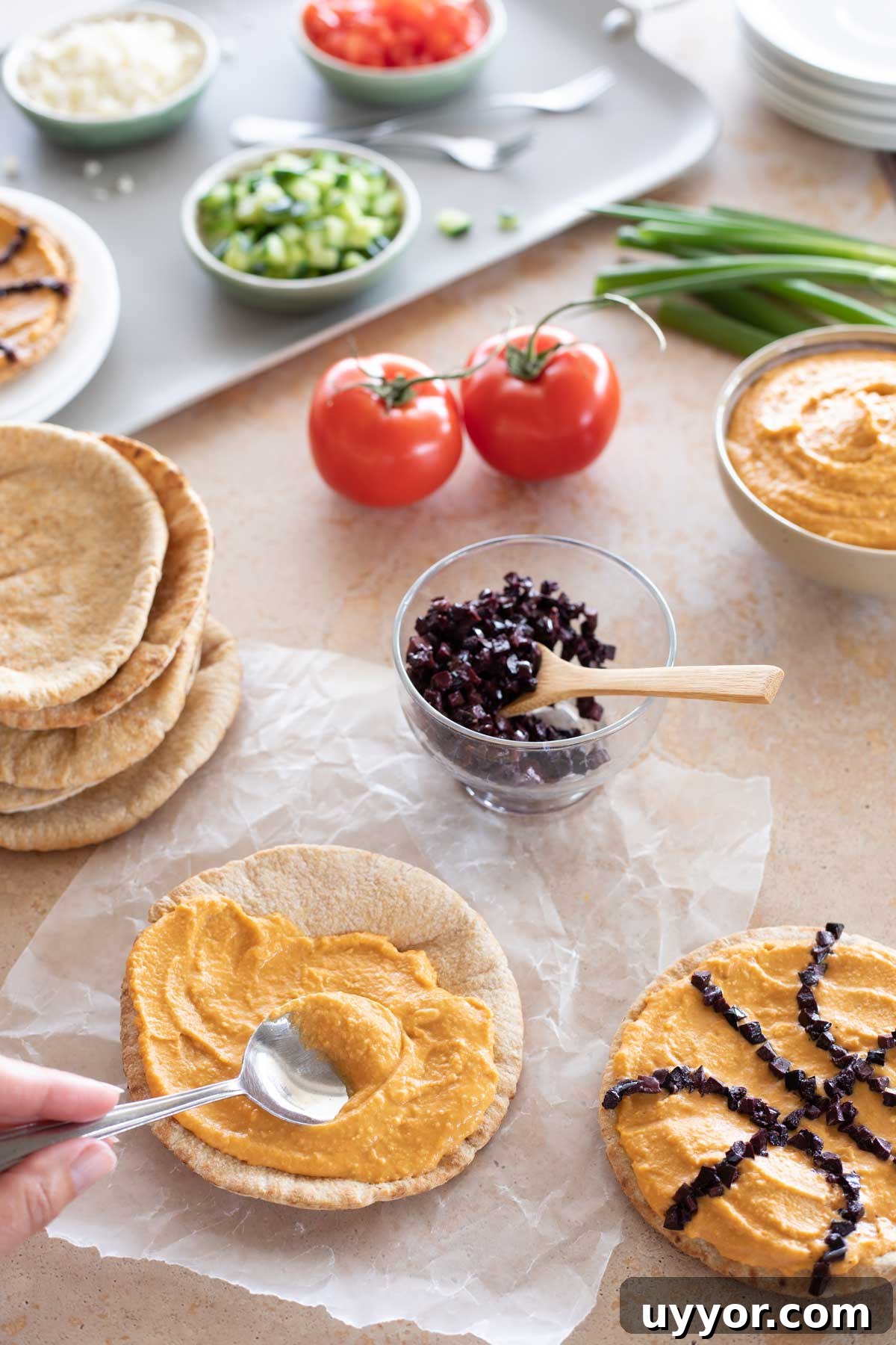 50+ Winning March Madness Game Day Recipes and Snacks 7 Fingers using spoon to spread hummus on pita, with other ingredients nearby.