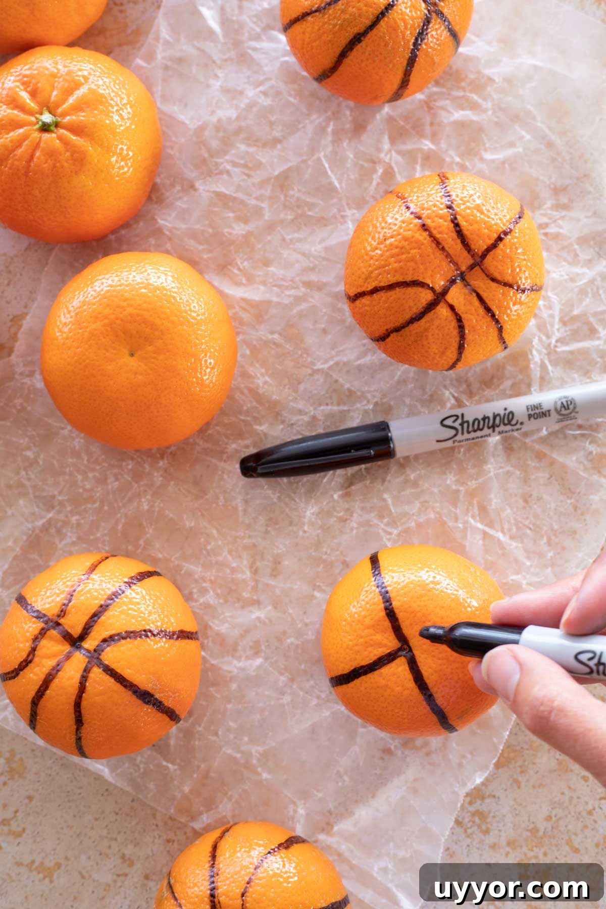 50+ Winning March Madness Game Day Recipes and Snacks 11 Fingers holding Sharpie to draw lines on clementine to look like a basketball.