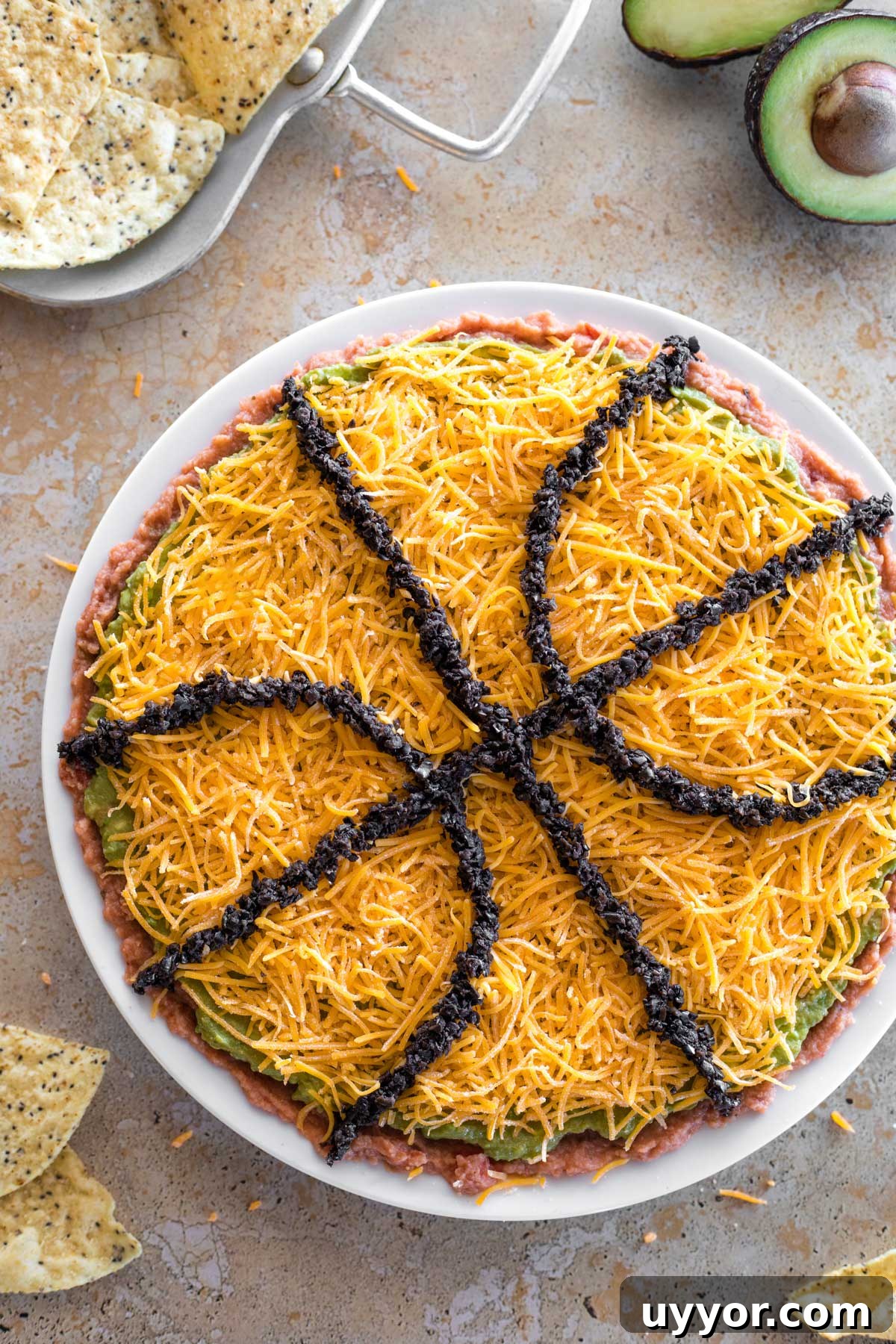 50+ Winning March Madness Game Day Recipes and Snacks 3 Overhead of finished March Madness layered dip, with tortilla chips and avocado halves decoratively in background.