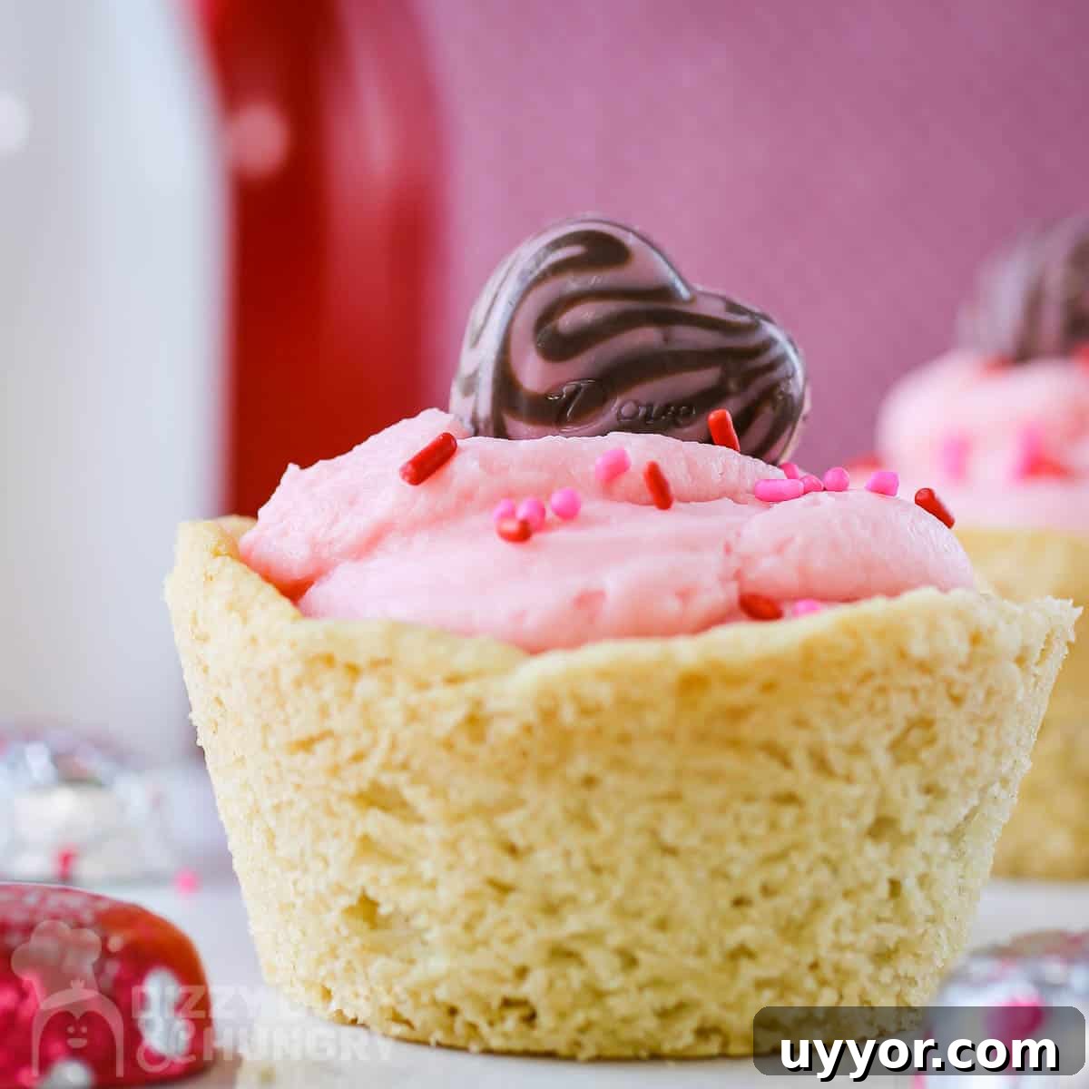 Strawberry Cream Cheese Cookie Cups: Soft Cookies Filled with Creamy Strawberry Centers 5 Close up shot of a cookie cup on a white plate with chocolate hearts scattered around with a pink background.