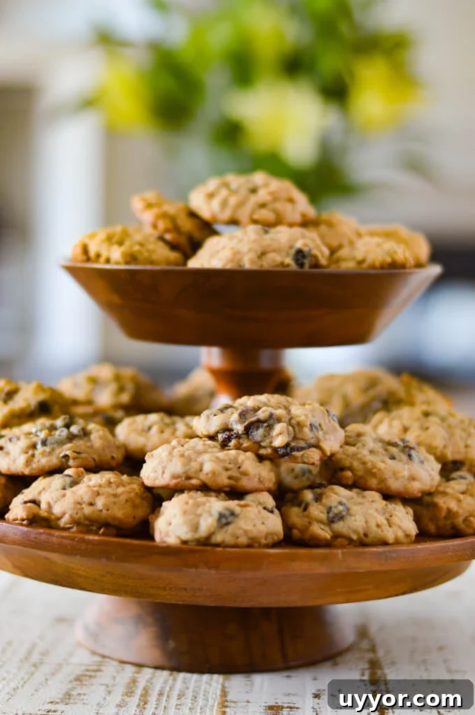 A tiered wooden platter full of oatmeal raisin cookies with a bouquet of flowers blurred in the background.
