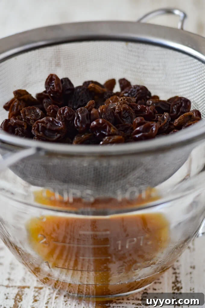 Boiled raisins draining in a wire strainer into a clear measuring cup.