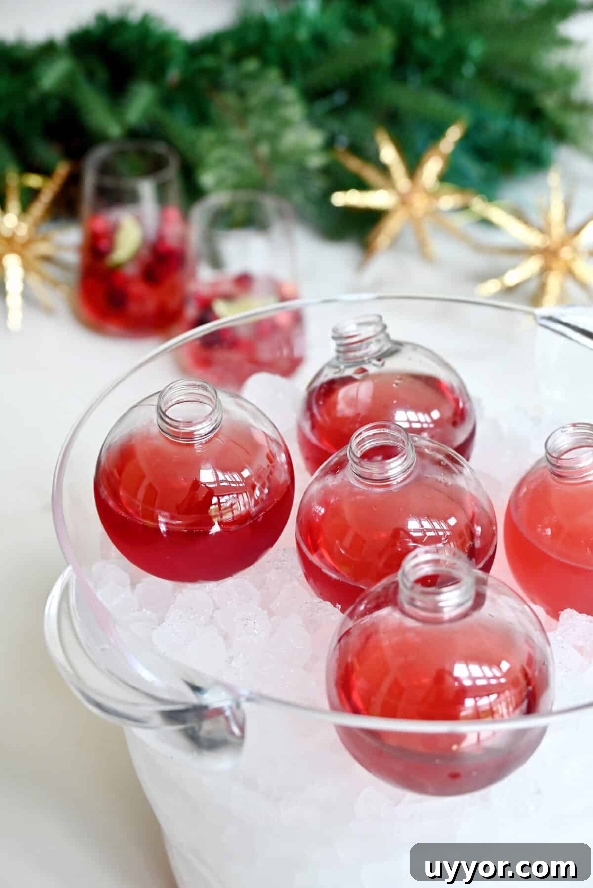 Clear ornament drinking balls filled with cranberry margaritas nestled in ice in a clear ice bucket.