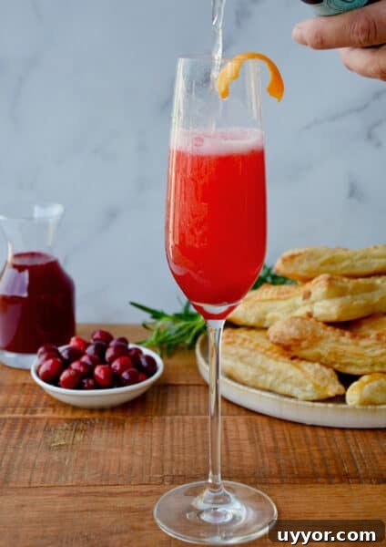 A person pouring Prosecco into a flute with cranberry syrup.
