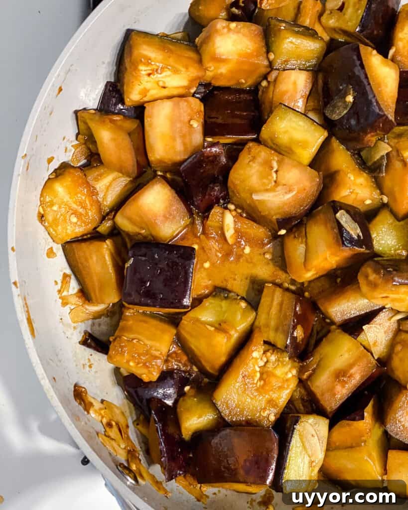 process shot of mixing sauce with eggplant in pan