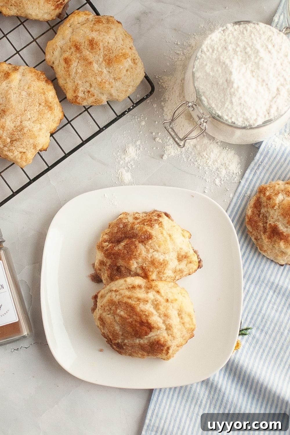 overhead view of cinnamon sugar biscuits with glaze, served on a white plate, with additional biscuits and flour in the background.