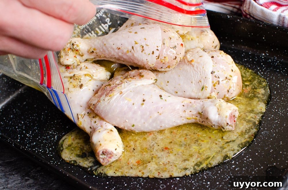 Pouring the marinaded chicken drumsticks onto a black baking tray