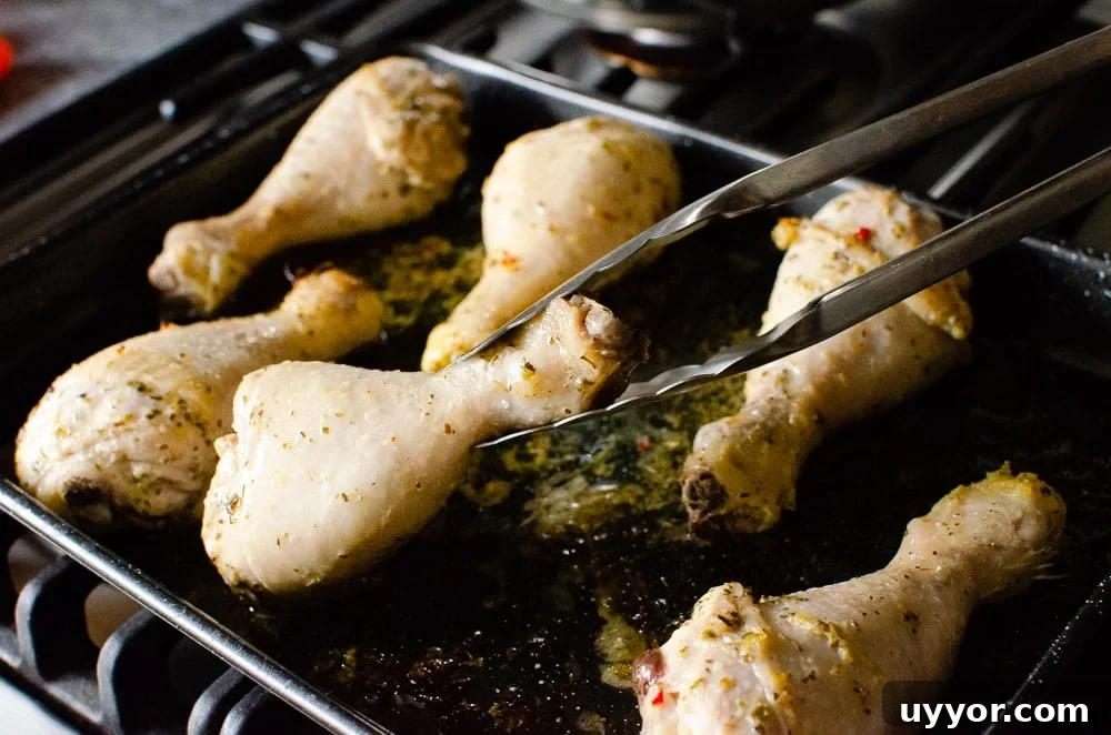 Turing the chicken drumsticks over with silver tongs