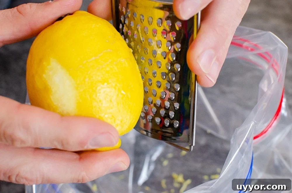 Grating lemon zest with a silver grater into a clear plastic sandwich bag