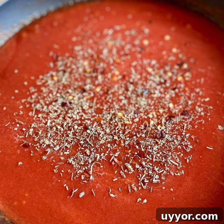 Tomato sauce in a black frying pan sprinkled with salt, chili flake, and Italian seasoning