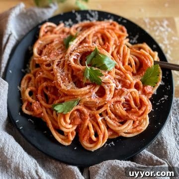 Twirled spaghetti on a black plate topped with parsley and parmesan cheese on a butcher block cutting board with a light gray linen