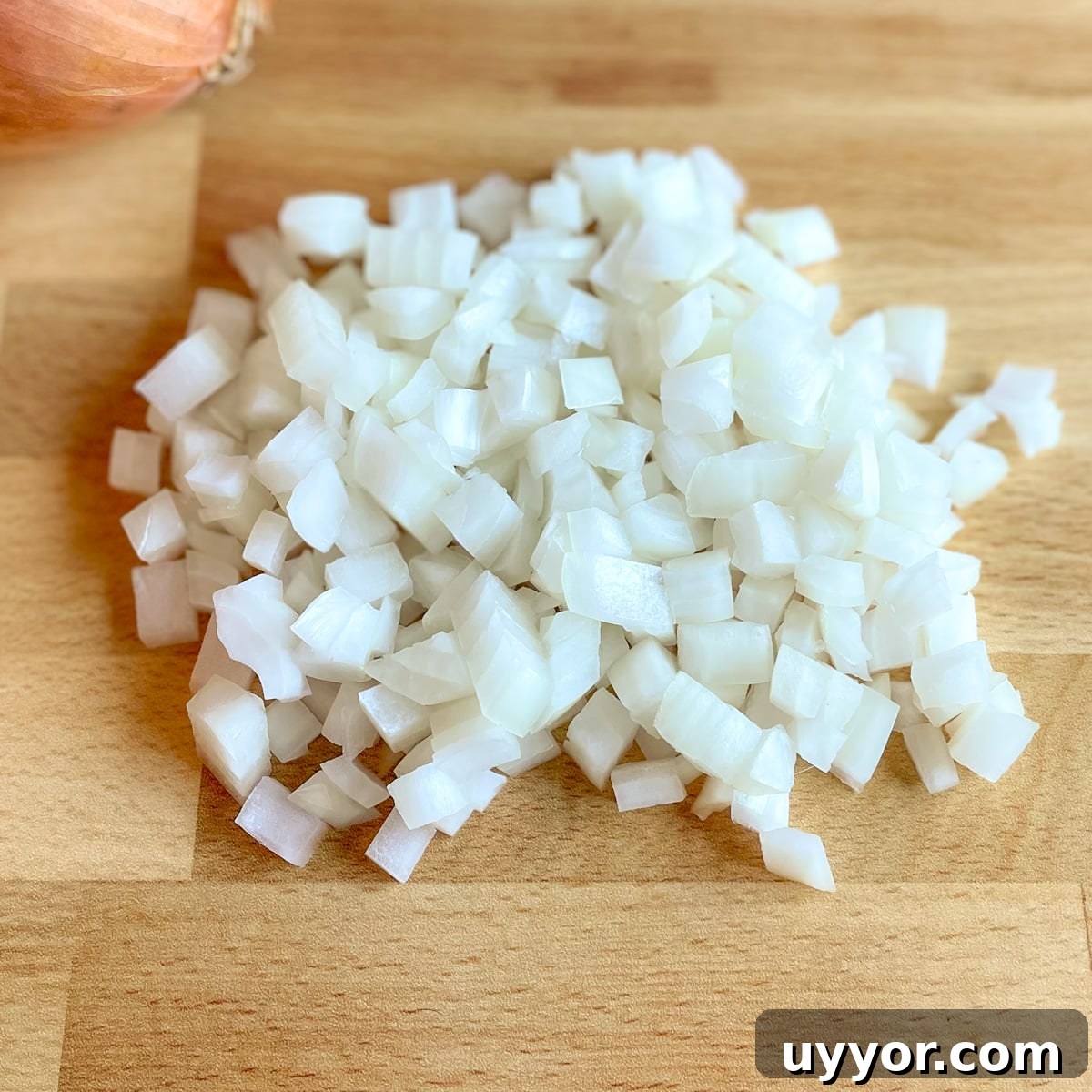 Diced yellow onion with a yellow onion in the background on a butcher block cutting board