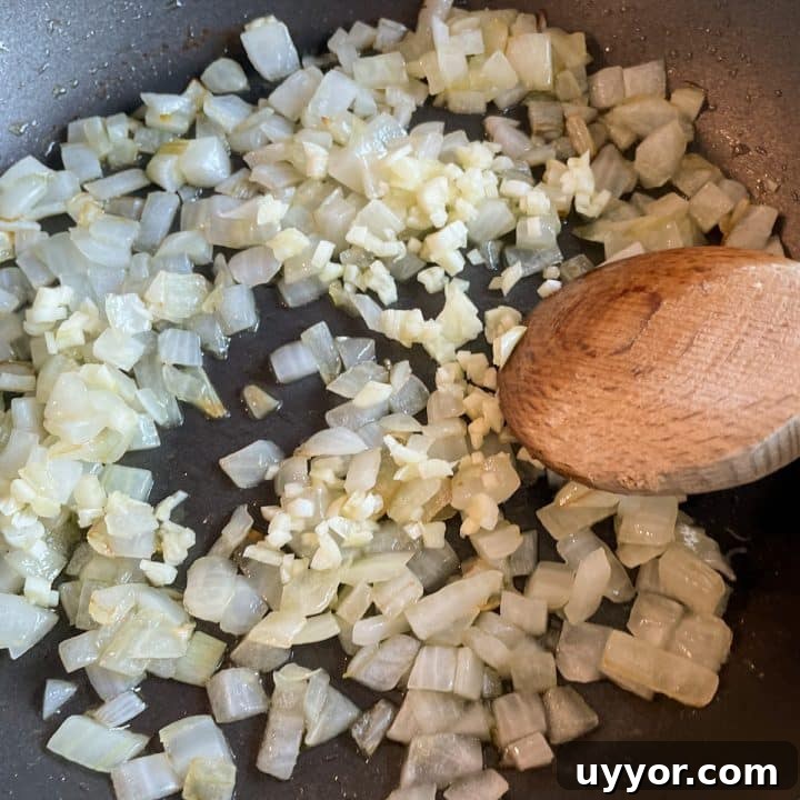 Sautéed onions and garlic in a black frying pan with a wooden spoon