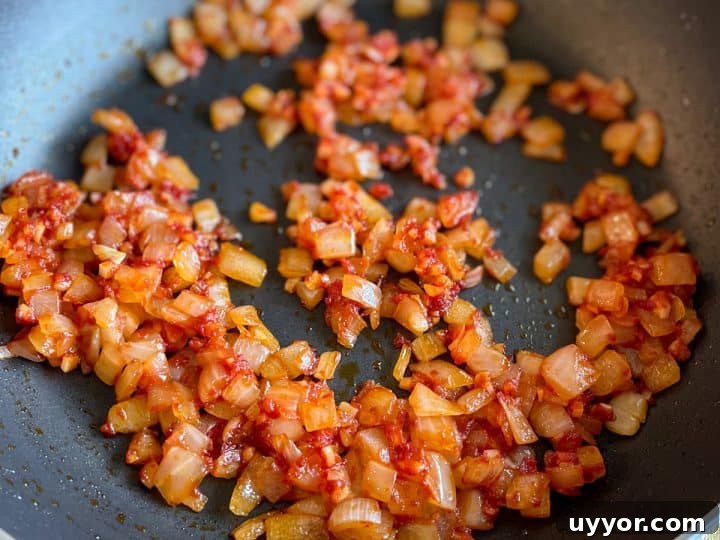 Sautéed onion, garlic, and tomato paste in a black frying pan