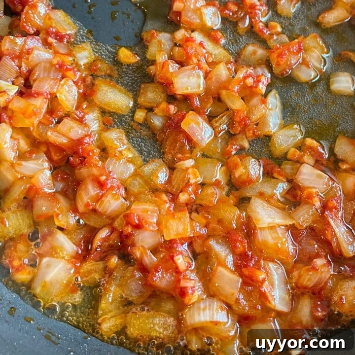 Sautéed onion, garlic, tomato paste, and white wine in a black frying pan