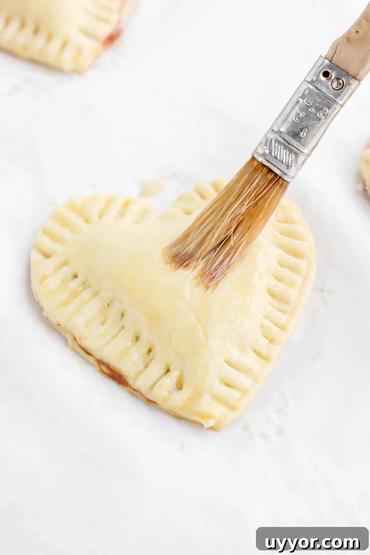 heart shaped pastry being brushed with egg wash.
