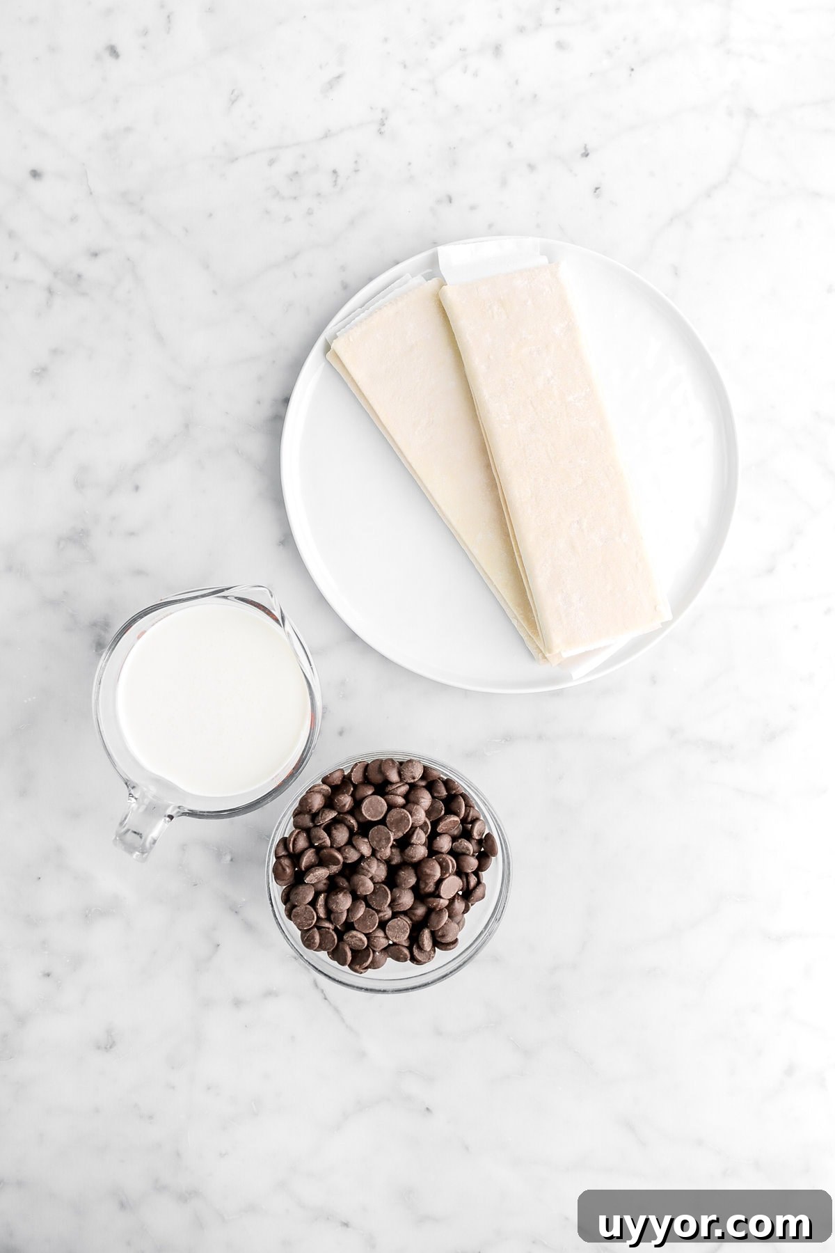 two sheets of puff pastry, heavy cream, and chocolate chips on marble surface.