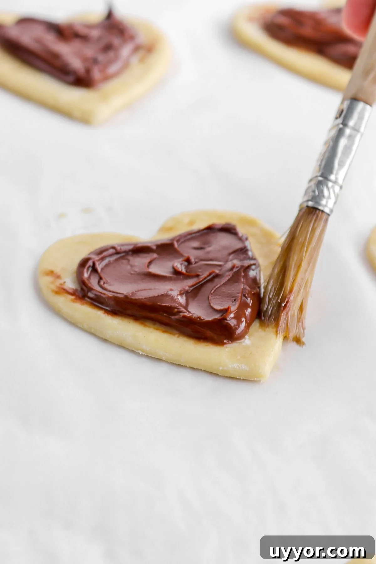 heart shaped pastry being brushed with egg wash.
