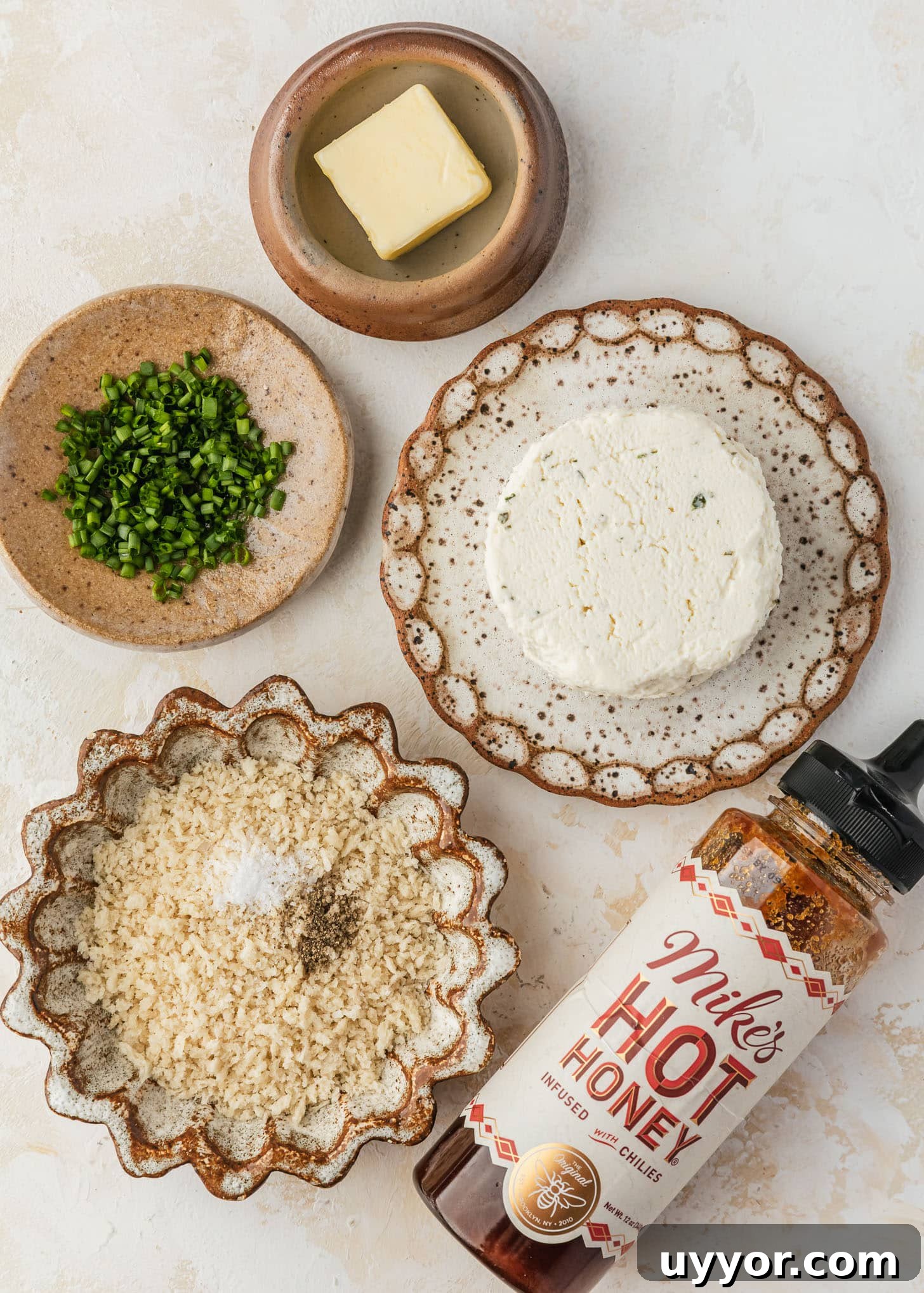 Crispy Baked Boursin Bites Without Dredging 3 White and brown plates of cheese, chives, butter, and breadcrumbs next to a bottle of hot honey on a tan table.