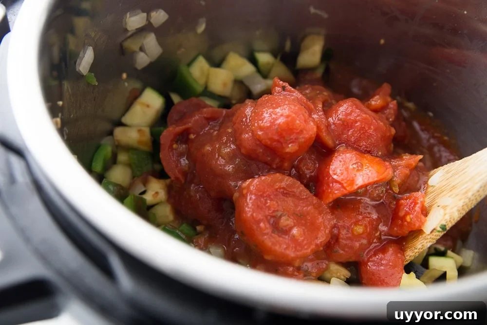 Instant Pot Ratatouille: Quick French Vegetable Stew Recipe 4 An instant pot full of veggies with a pile of canned tomatoes just added - wooden spoon resting on the side, ready to stir
