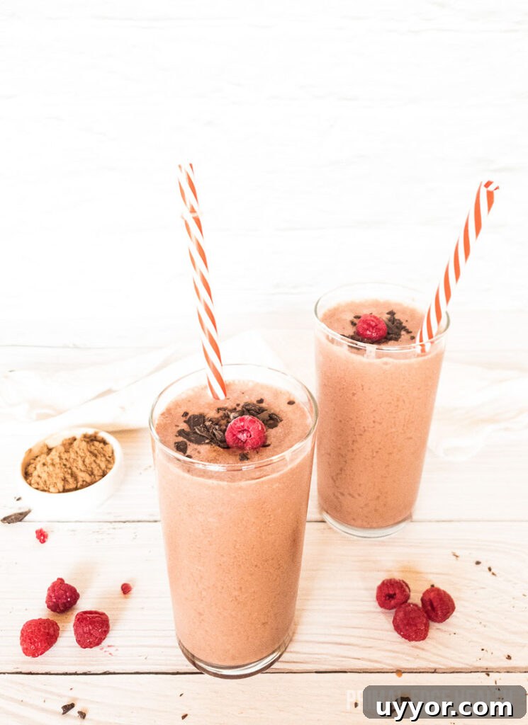 Chocolate raspberry smoothie in a glass with straw on a wooden surface.
