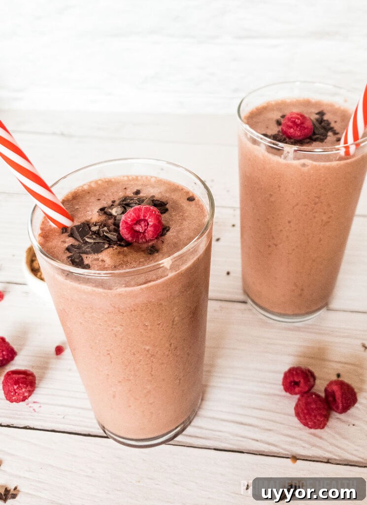 Two glasses of chocolate raspberry smoothie on a wooden surface.