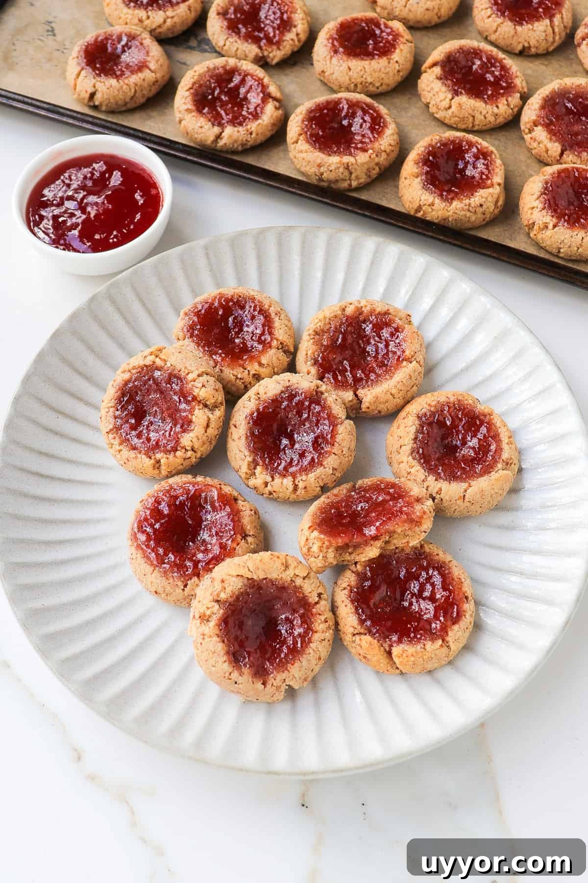 Strawberry jam thumbprint cookies on a plate. One cookie with a bite missing.