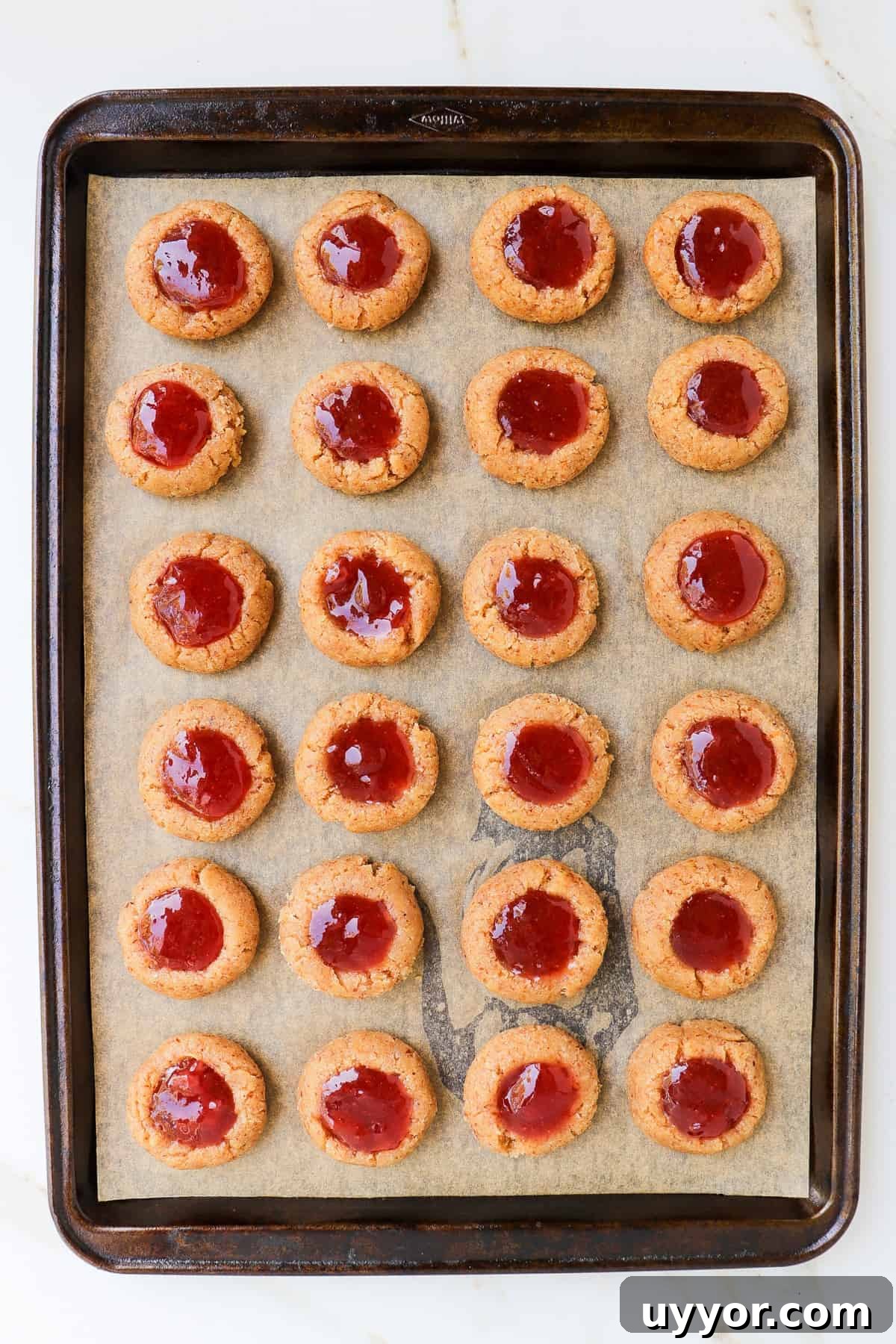 Raw cookies on baking tray filled with strawberry jam before the oven.