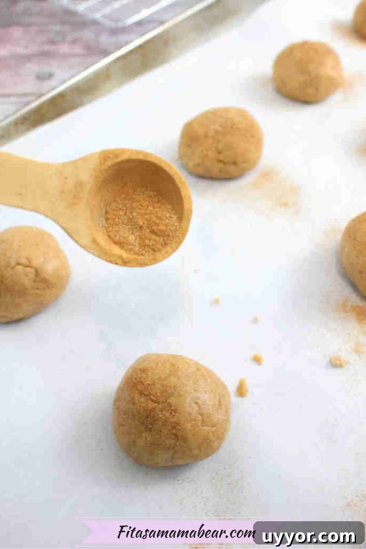Cinnamon sugar being sprinkled on Snickerdoodle protein cookies on a baking sheet.