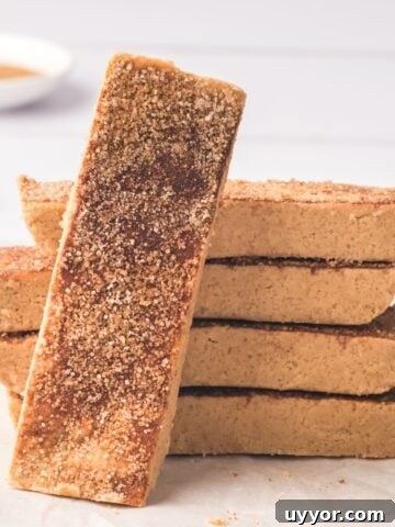 Snickerdoodle protein bars stacked with one bar in front and cinnamon sticks and milk behind it.