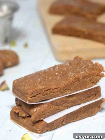 Three gingerbread protein bars stacked with parchment paper between them and pistachios around them.