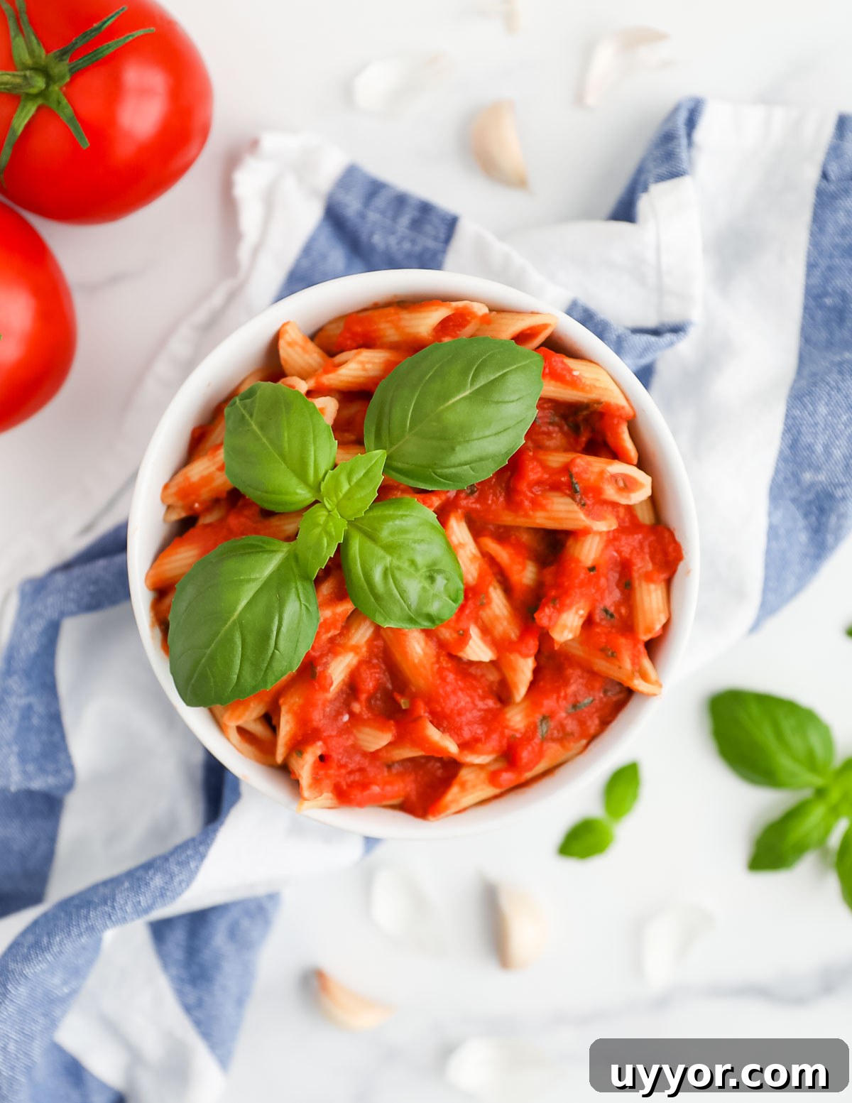 A white bowl filled with pasta with a red sauce, garnished with fresh basil.