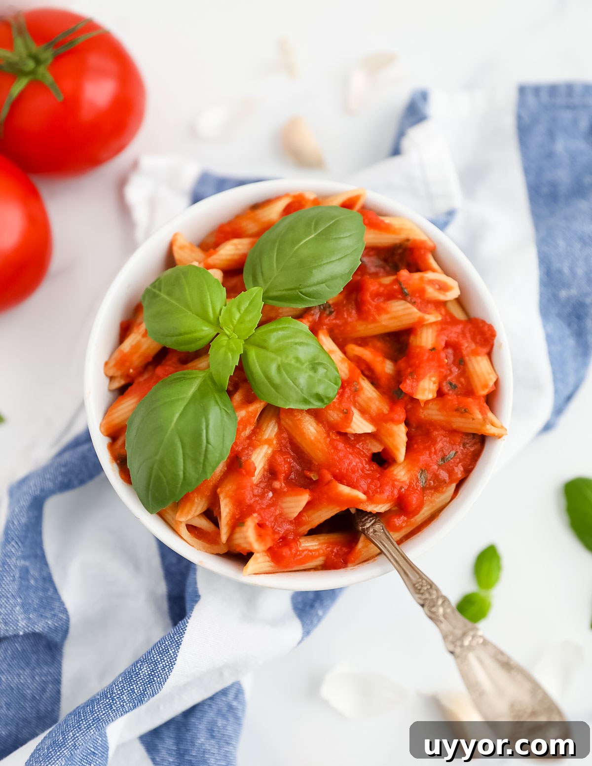 A bowl of penne pasta with pomodoro sauce garnished with a fork and a fresh sprig of green basil