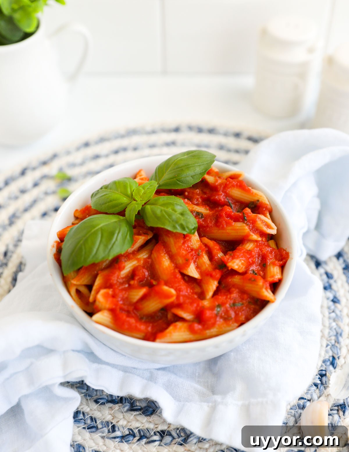 Penne pasta with red pomodoro sauce in a white bowl, garnished with bail.