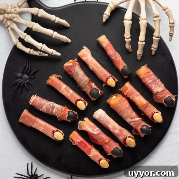 Savory Halloween witch fingers on a black serving board with skeleton hands reaching in.