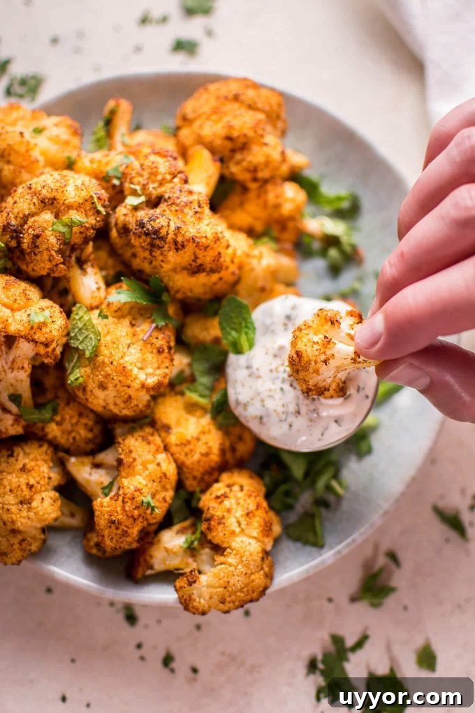 Roasted Cauliflower Bites with Cooling Mint Yogurt Dip 6 a hand dipping a roasted cauliflower bite into container of mint dipping sauce