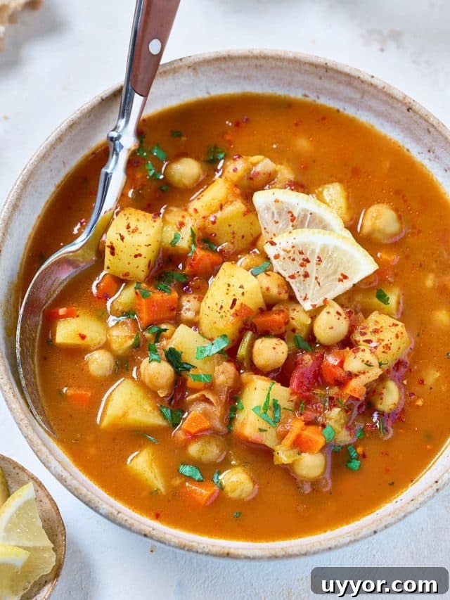 A spoon scooping chickpeas and vegetable soup from a bowl.
