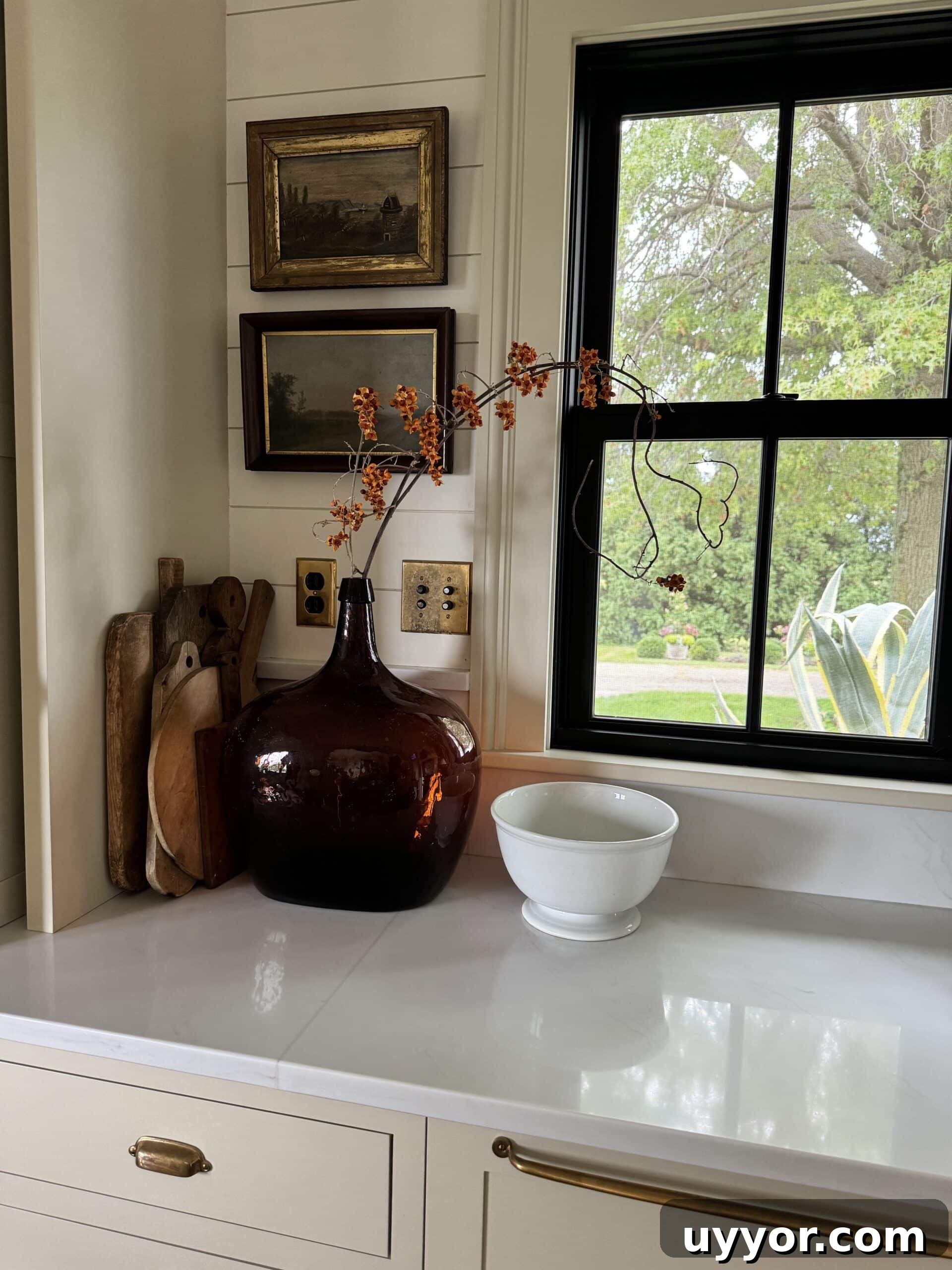 August 2024 Events, Deals & Planning Guide 3 Kitchen countertop with large amber vessel with sprig of bittersweet in front of window.