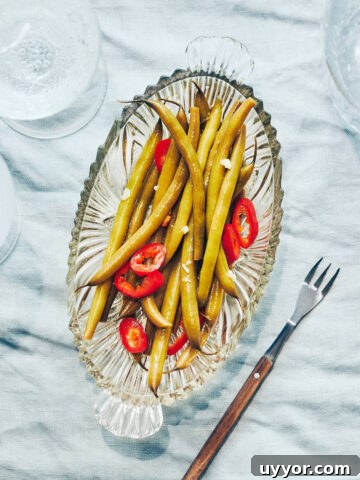 Plate of pickled green beans and peppers on a table with sparkling water on the side