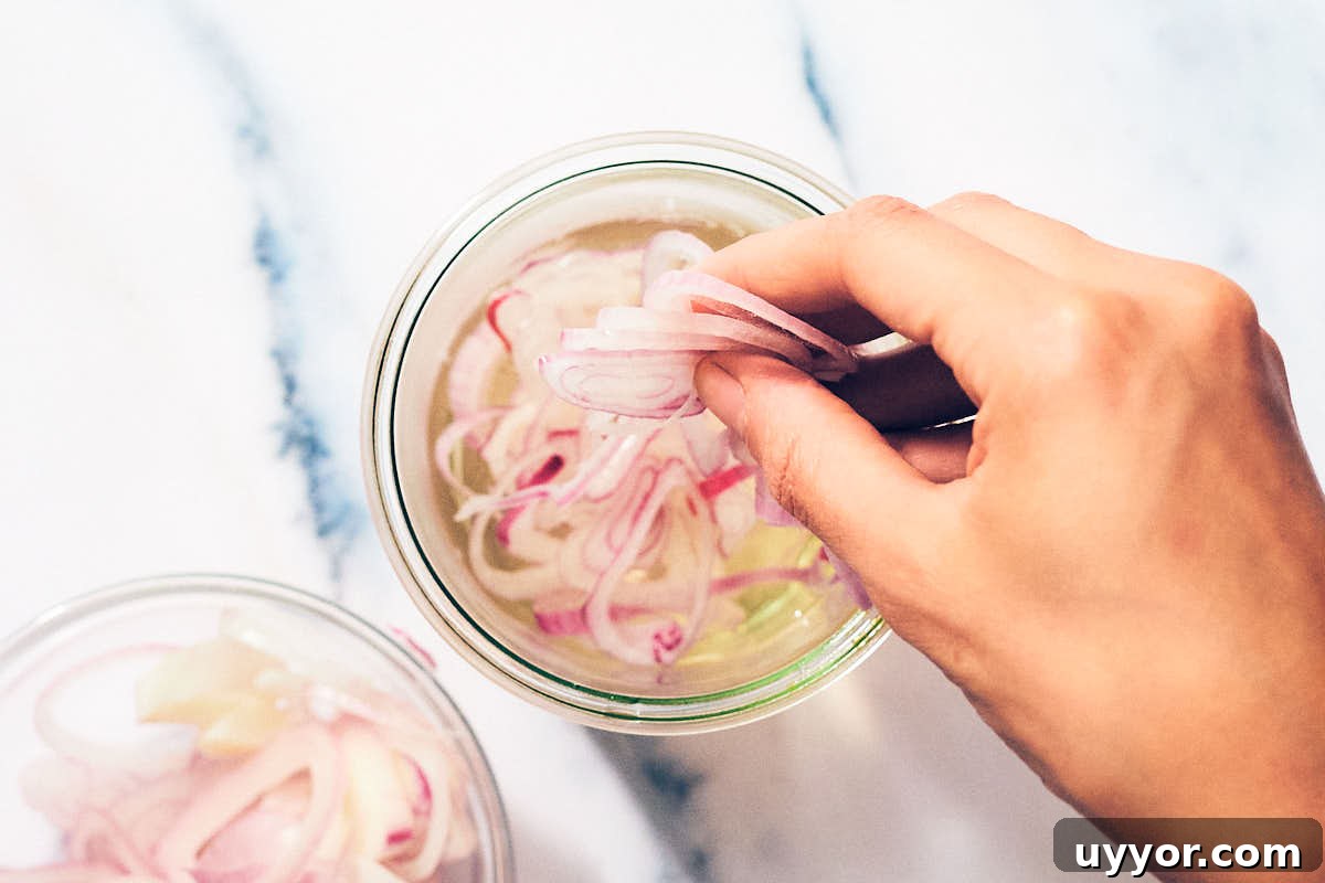 Thinly sliced shallots being added to vinegar brine to quick pickle.