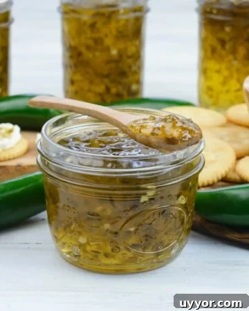 An open canning jar of Jalapeno Pepper Jelly with a spoon, more jars in the background.