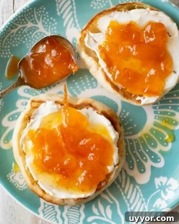 Toasted English Muffins with cream cheese and peach orange marmalade spread over the top on a teal glass plate.
