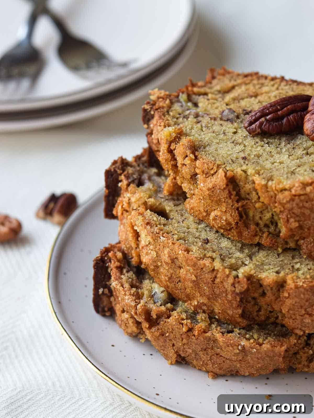 Bakery-Style Banana Bread with Pecans and Brown Butter Glaze 2 Three slices of banana bread stacked on a plate with pecans in the background.