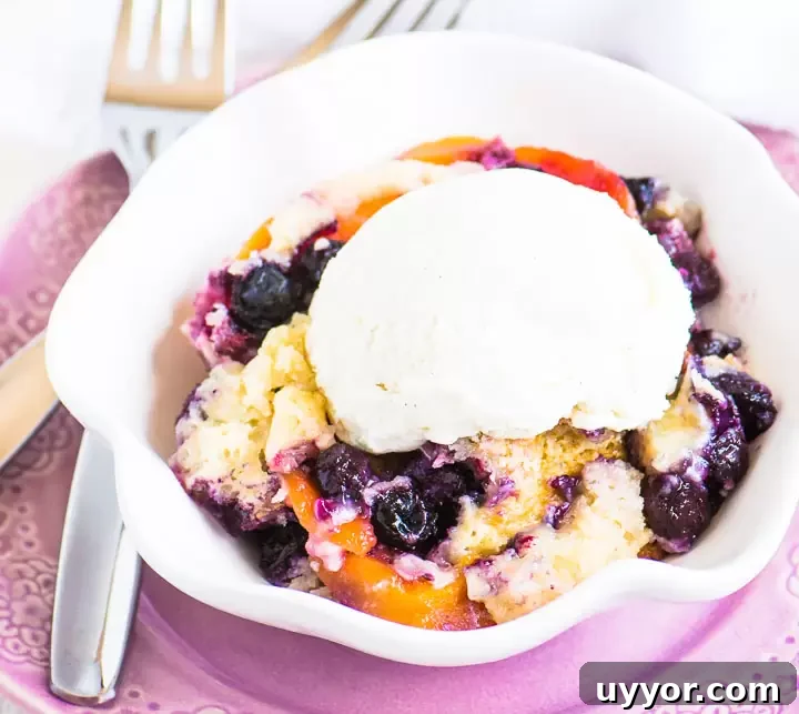 Perfect Blueberry Peach Cobbler Recipe for Summer Desserts 2 scoop of cobbler in a bowl with ice cream on top and two forks next to it